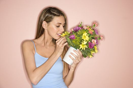 Caucasian mid-adult female holding pot of flowers and smelling them.