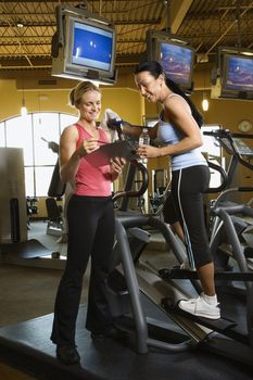 Prime adult Caucasian female on elliptical machine at gym with trainer.