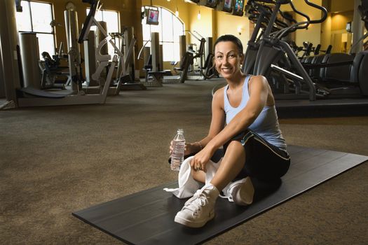 Prime adult Caucasian female sitting on mat on gym floor.