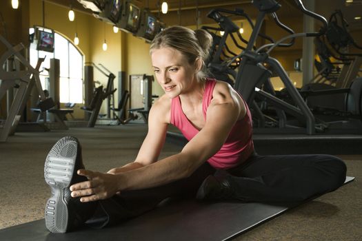 Prime adult Caucasian female stretching on mat in gym.