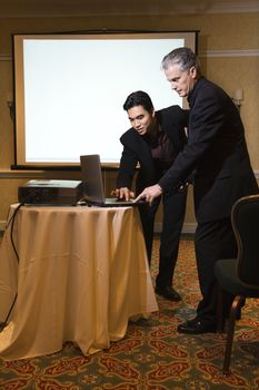 Asian prime adult businessman helping prime adult Caucasian businessman give presentation.