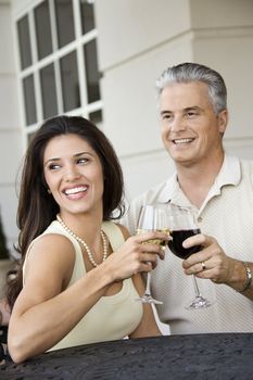 Prime adult Hispanic female and Caucasian prime adult male toasting sitting at table.