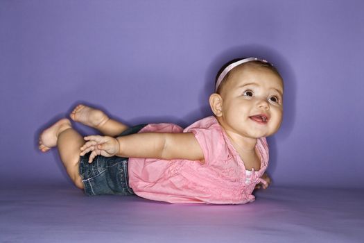 Hispanic female baby lying on stomach.