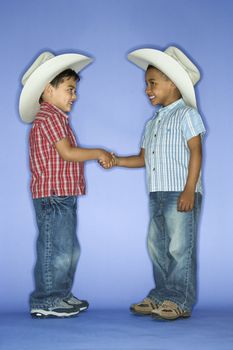 Hispanic and African American male child in cowboy hats shaking hands.