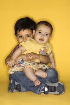 Hispanic and African American male child in cowboy hats shaking hands.