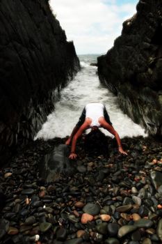 a beautiful woman practicing her yoga on the rocks in a ravine as the waves roll in