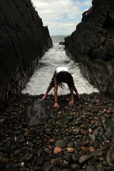 a beautiful woman practicing her yoga on the rocks in a ravine as the waves roll in