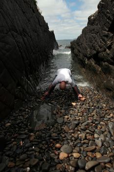 a bald man practicing his yoga on the rocks in a ravine as the waves roll in