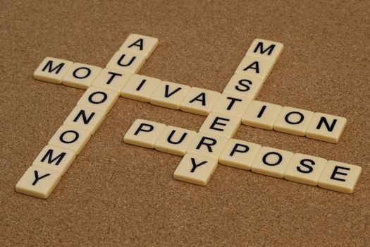 three elements of true motivation - mastery, autonomy, purpose - crossword with ivory letter blocks on cork board