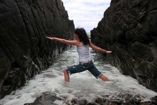 a beautiful woman practicing her yoga on the rocks in a ravine as the waves roll in