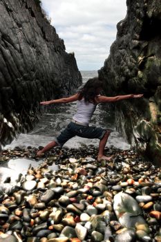 a beautiful woman practicing her yoga on the rocks in a ravine as the waves roll in