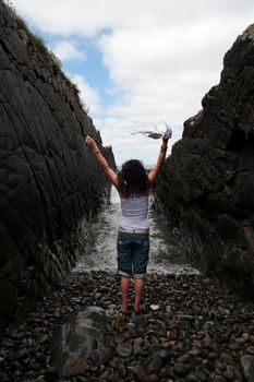 a beautiful woman waving her bra in the air as an expression of feeling free on the rocks in a ravine as the waves roll in