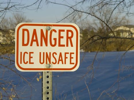 danger ice unsafe warning sign with a frozen pond in background