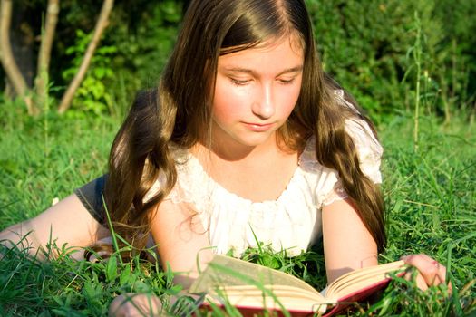 The young girl reads the book, laying on a grass