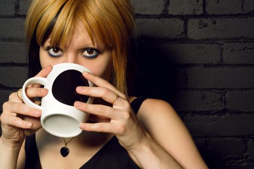 Female drinking coffee against the black brick wall of a urban café.
