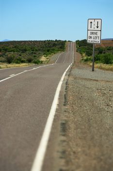 A road sign in the outback that warns, Drive on left in Australia.  Focus is on the sign - landscape is slightly out of focus.
