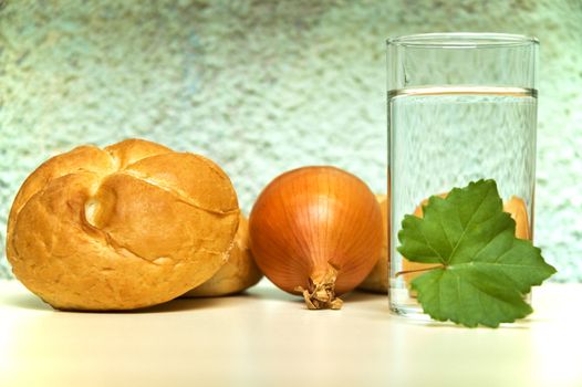 Bread roll, onion and glass of water on kitchen table.