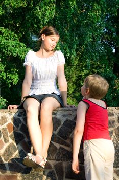 Children in park. The enamoured boy looks at the girl. The girl looks at the boy and smiles