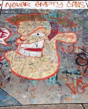 A photograph of extensive graffiti in an English skate park, with the words Never Empty Cans and a graffiti character's face, along with tags and other markings