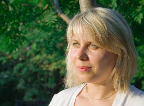 Portrait of the happy beautiful young woman-blonde against trees