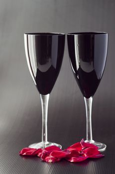 Two black glasses for wine over black background, with petals of rose