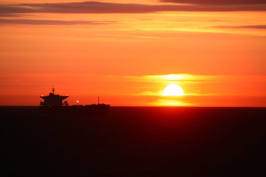 a sunrise on the open sea with ship in the background