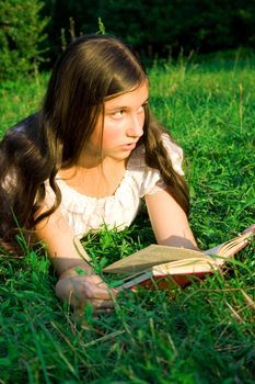 The young girl reads the book, laying on a grass