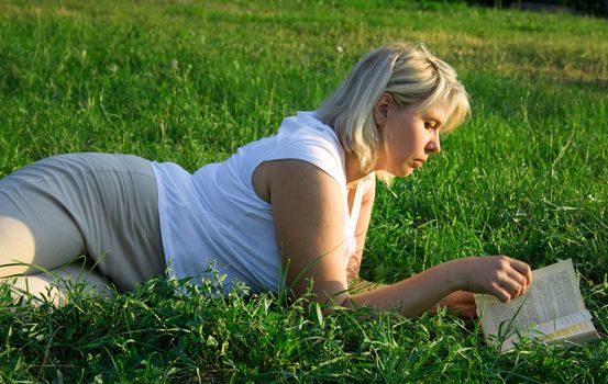 The young woman reads the book, laying on a grass