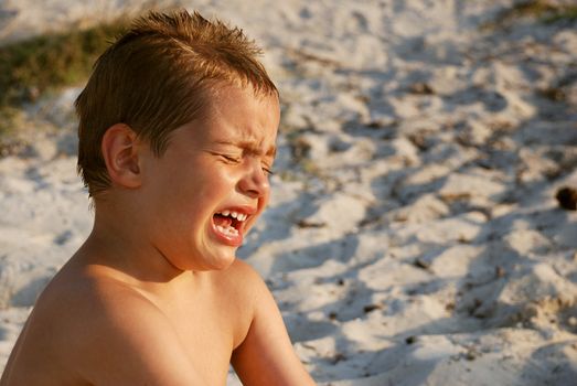 a boy is crying while sitting in a sand