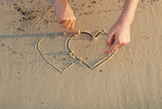 a girl is drawing hearts in a sand