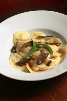 A plate of heart-shaped homemade ravioli smothered in butter and sage herbs.
