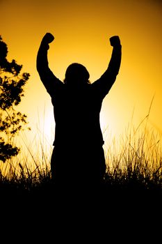 A person in silhouette at sunset with their hands in the air
