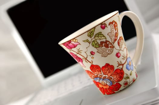 Coloured mug sitting on white laptop. Symbolizing a coffee break