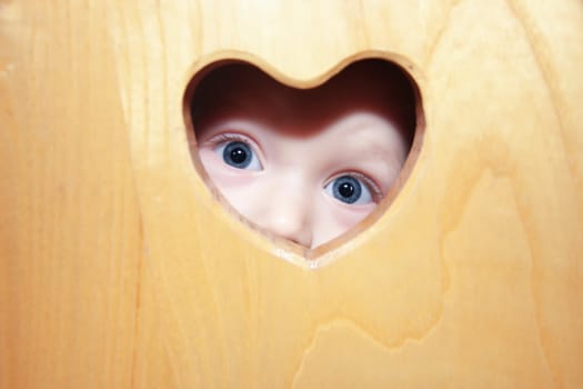 Yound boy with blue eyes looking through heart shaped hole