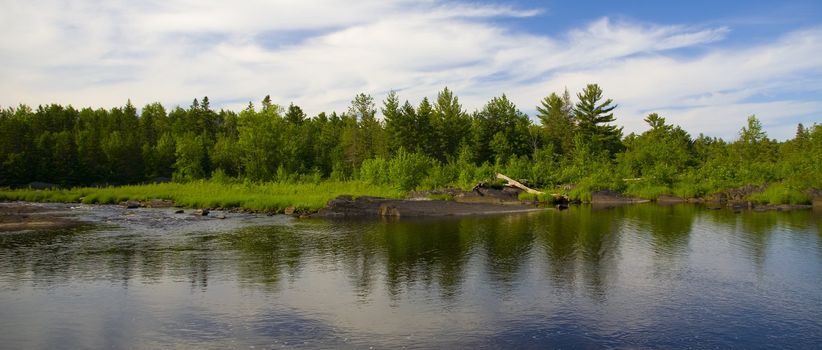 Forest of the North Woods of Minnesota across the reflection of a still river.