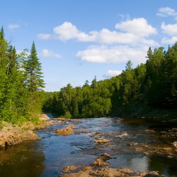 River flows slowly above a large waterfall in the North Woods of Minnesota.