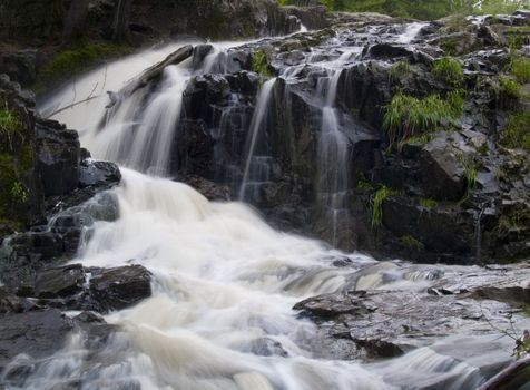 A waterfall and rapid creek falling around a stone face Northern Minnesota.