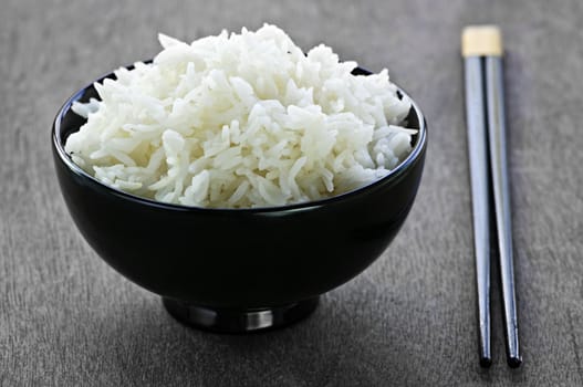 White steamed rice in black round bowl with chopsticks