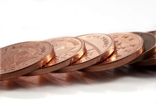 Close and low level capturing a line of British copper coins arranged over white.