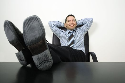 Photo of a happy businessman reclining with his feet up and hands behind his head.