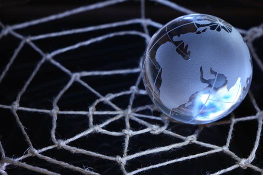 Glass globe lying on web made from rope on dark background