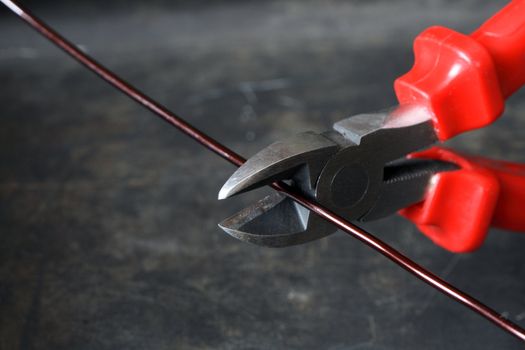 Closeup of wire-cutter and wire on dark metal background