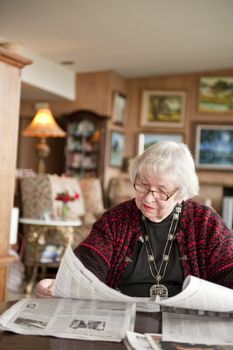 87 year old woman at home reading paper. USA