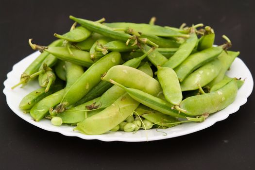 Peas pods on a white plate on a black background