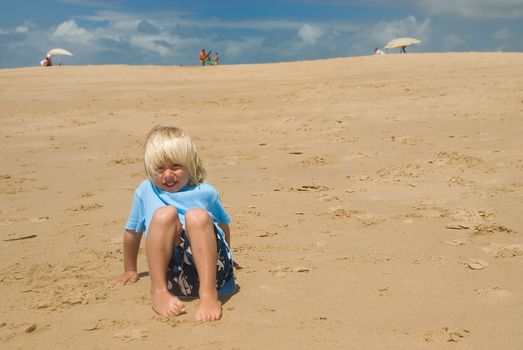 a boy sitting on the beach on a sunny day