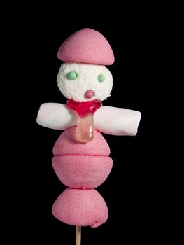 A male figurine made out of candies on a stick over a black background.