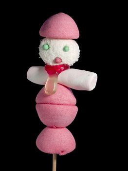 A male figurine made out of candies on a stick over a black background.