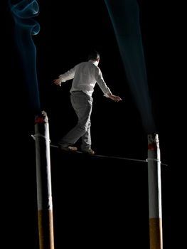 A man walking a tightrope suspended  between two big cigarettes. A conceptual image about the health risks of smoking.