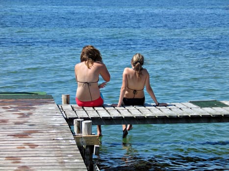Two girls sit and relax on a dock near the sea in Denmark
