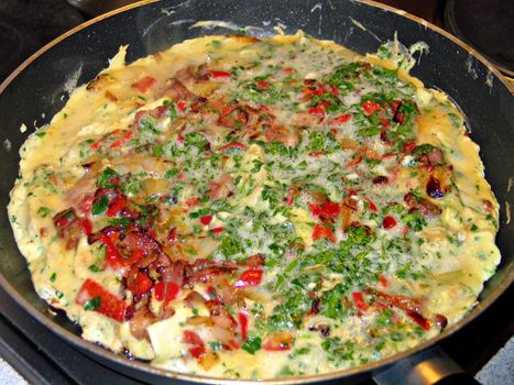 Omelette with ham and fresh vegetables in a frying pan